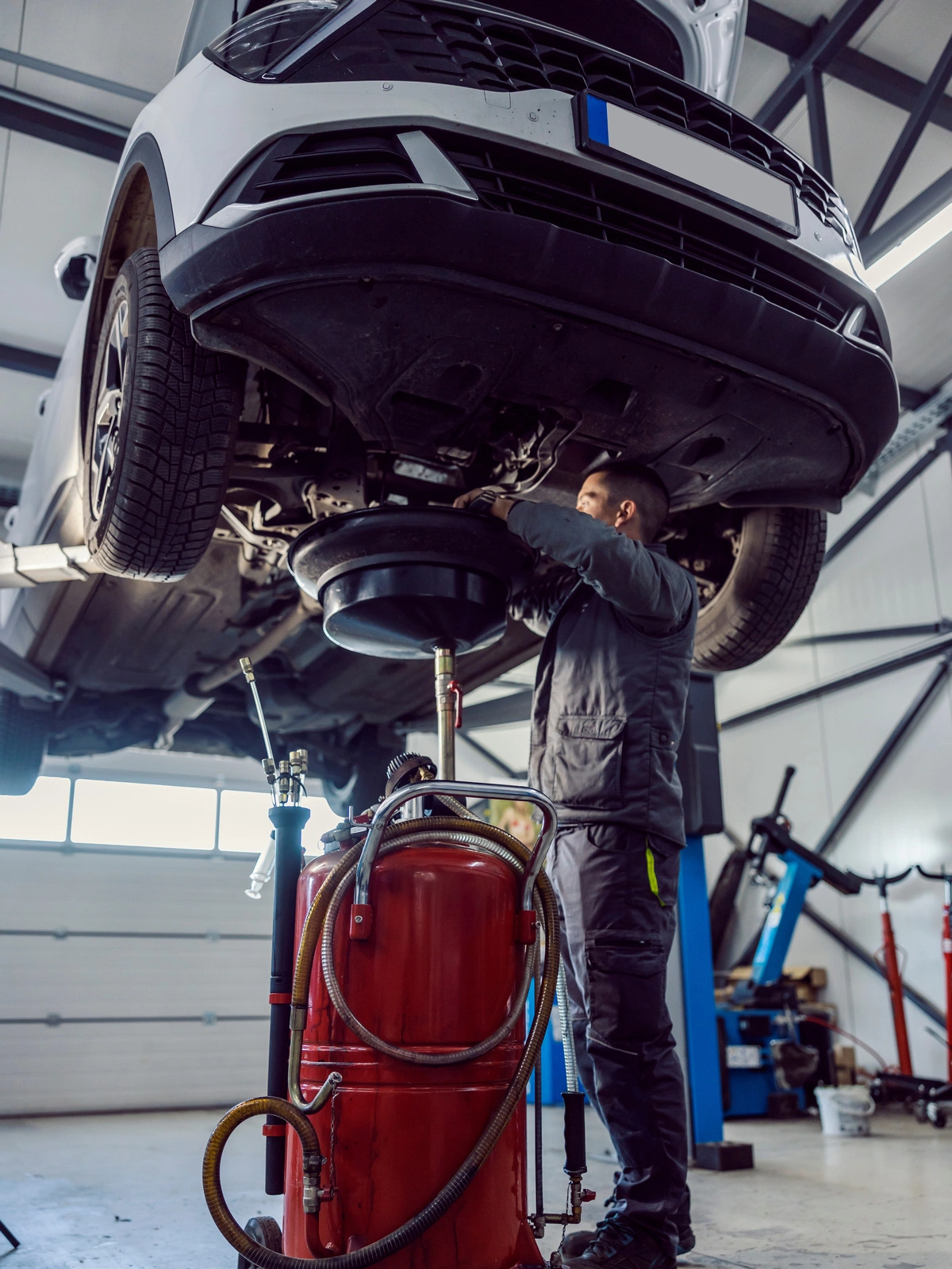 Entretien voiture professionnel : mécanicien travaillant sous un véhicule surélevé dans un atelier équipé pour la maintenance automobile