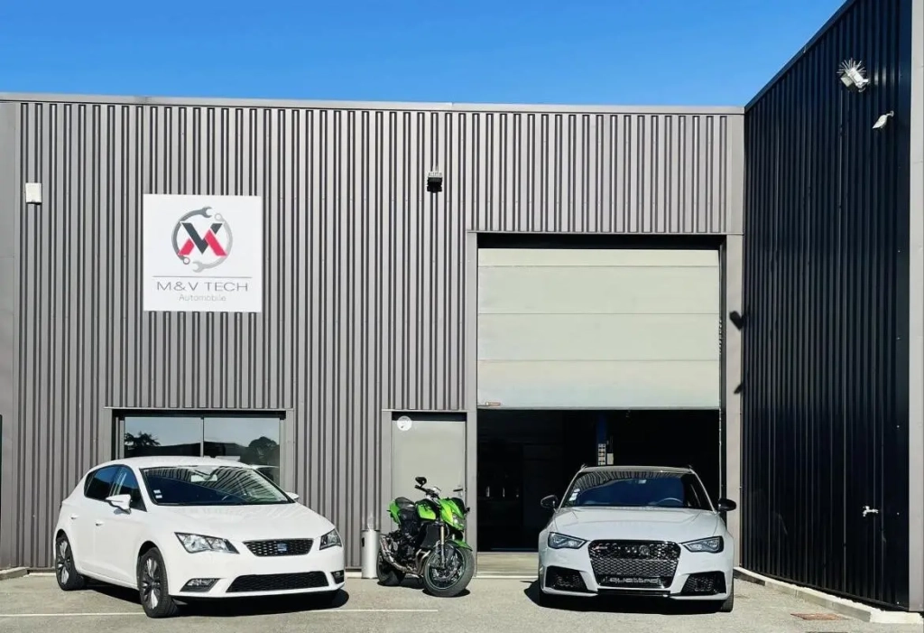 Façade du garage M&V Tech avec son logo, une porte de garage et trois véhicules garés devant : deux voitures blanches et une moto verte